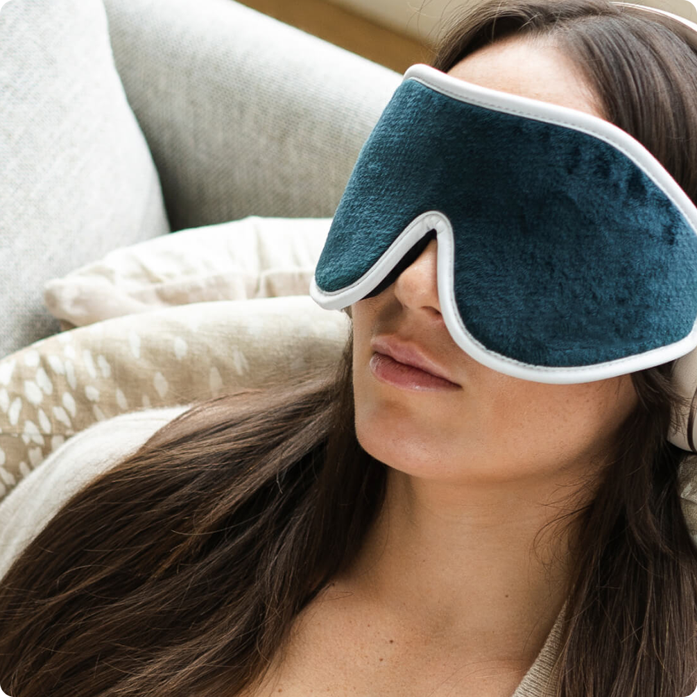 A woman relaxing on a couch wearing a plush sleep mask.
